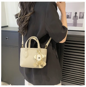 Detail of beige lychee texture bucket bag featuring a unique monkey leather charm