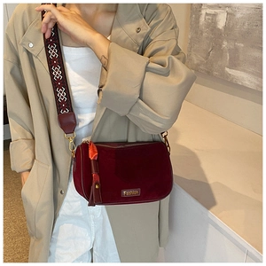 Close-up of a burgundy velvet pillow bag featuring a patterned strap and gold logo