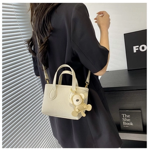 Detail of off-white lychee texture bucket bag with bear charm on black blazer