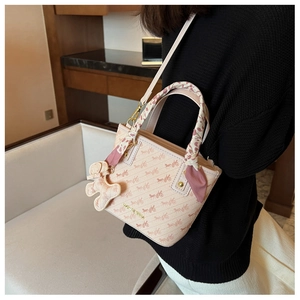 Detail of pink crossbody bucket bag with horse print, silk scarf, and bear charm accessory