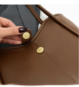 Close-up of golden round magnetic closure on brown leather tote bag detail