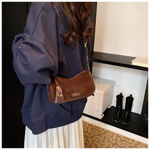 Model wearing a retro dark brown suede crescent shoulder bag with a gold metal logo tag