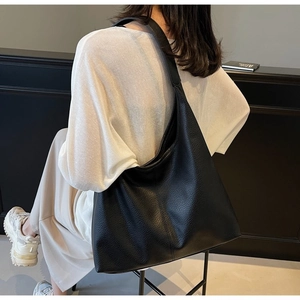 Detailaufnahme einer schwarzen Tragetasche mit Litschimuster, getragen von einem Modell
