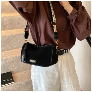 Close-up of black suede pillow bag with a geometric pattern strap and gold hardware