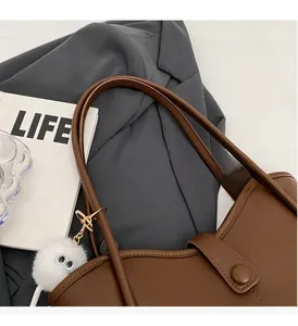 Detail of brown leather tote bag featuring a white furry monster charm and golden hooks