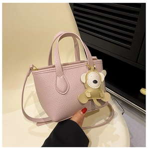 Pink litchi texture bucket bag with a cute monkey charm placed on a beige chair