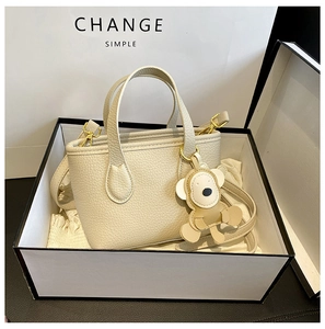 Detail of off-white lychee leather bucket bag with bear charm and golden hardware