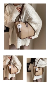 Close-up of beige tote bag with brown trim and cute white plush pendant accessory