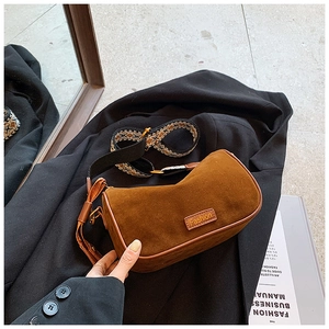 Detail of dark brown suede pillow bag with embossed label and geometric woven strap