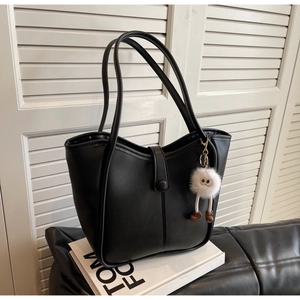 Detail of black faux leather tote with white plush toy charm and snap closure