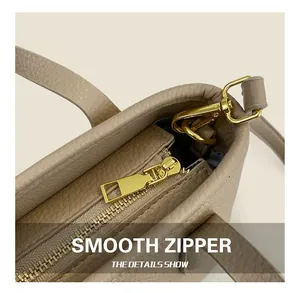 Detail of smooth gold zipper and lychee leather texture on a beige bucket bag