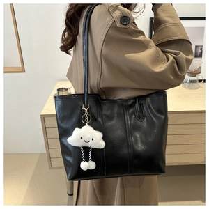 Dettaglio di una borsa tote nera capiente con trama in pelle e ciondolo a nuvola di peluche