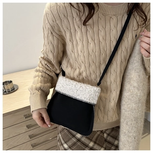 Detail einer flauschigen Beuteltasche mit weißem Plüschbesatz und schwarzem Korpus am Strickpullover