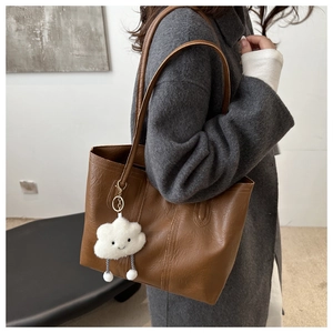 Dettaglio della borsa tote marrone con ciondolo a nuvola di peluche sulla maniglia