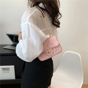 Pink quilted crossbody chain bag with V-shaped stitching shown on a person