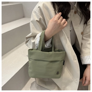 Detail of pea green fabric bucket bag featuring a round metal logo and woven texture