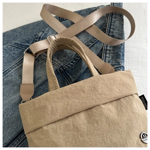 Detalle del bolso tote de nailon plisado caqui con logo M de metal sobre tela vaquera