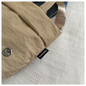 Primer plano de la textura de nailon plisado con logo metálico y etiqueta en el bolso