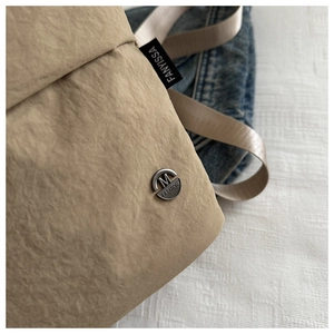 Detalle de la tela plisada caqui con etiqueta FANYISSA y emblema plateado M FASHION