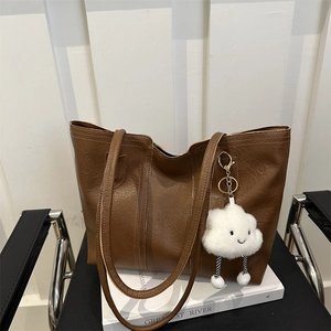 Borsa tote in pelle marrone con ciondolo a nuvola di peluche in set fotografico