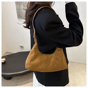 Brown suede crescent bag shown with adjustable strap over a black blazer on model