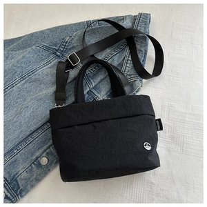 Close-up of minimalist black bucket bag with silver metal logo and side woven label