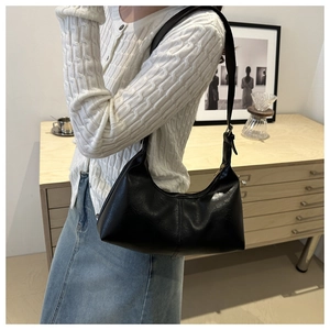 Side view of black crescent underarm bag in glossy leather worn with casual cardigan