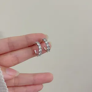 Detail view of silver C-shaped earrings with clear cubic zirconia held by hand