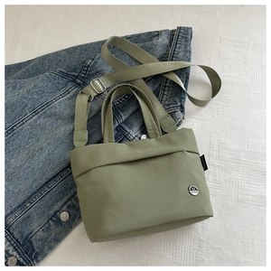 Detail of sage green nylon bucket bag featuring a metal logo and adjustable strap