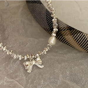 Detail of silver beaded bracelet with a glossy bow charm and a single white pearl accent