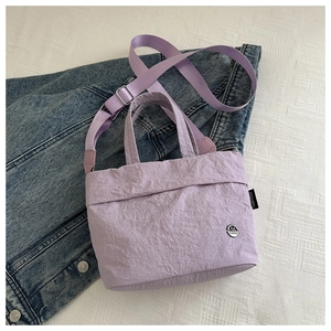 Macro detail of lavender pleated tote bag with metal M logo on denim jacket