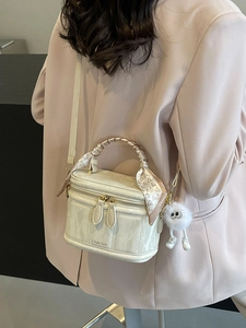 Minimalist beige box bag with silk scarf handle and plush monster charm in a crossbody style