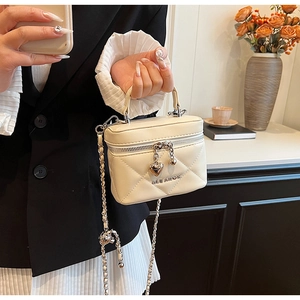 Close-up of cream quilted bag with chain strap and heart charm detail on zipper
