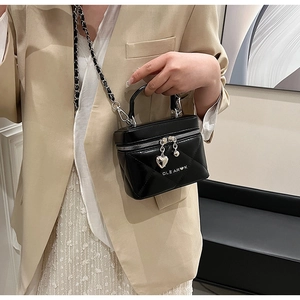 Detail of black quilted bucket bag featuring heart charms and metal chain strap