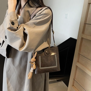 Bolso tipo cubo retro marrón con correa tejida y colgante de conejo en modelo