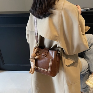 Bolso tipo cubo retro de cuero marrón con costuras blancas y correa de jacquard