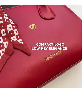 Nahaufnahme der roten Ledertasche mit goldenem Herz-Logo und elegantem Seidenschal-Detail