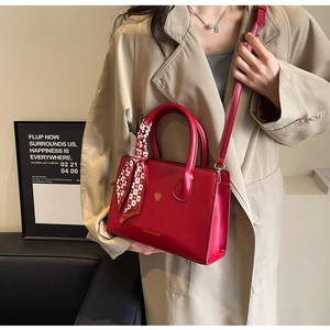 Detail der roten Ledertasche mit Herz-Beschlägen und dekorativem rot-kariertem Seidenschal