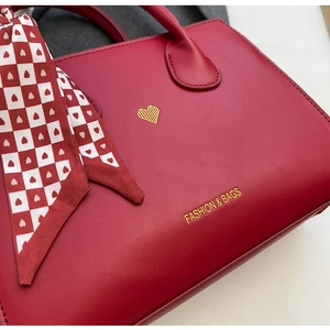 Detailansicht rote Lederhandtasche mit goldenem Herzdekor und dekorativem Seidenschal