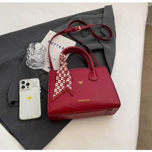 Detail der roten Ledertasche mit Herzanhänger und Seidenschal auf grauem Anzug-Blazer