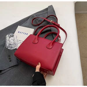 Detailansicht einer roten Henkeltasche mit Seidenschal-Deko auf einem grauen Sakko