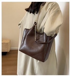 Detail view of large dark brown quilted tote bag with golden chain strap on a shoulder