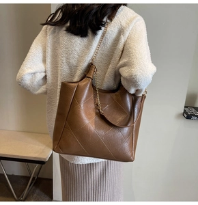 Detail view of large brown quilted tote bag with gold chain strap on model shoulder