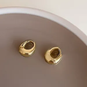 Détail macro de boucles d'oreilles goutte dorées polies sur un plateau céramique