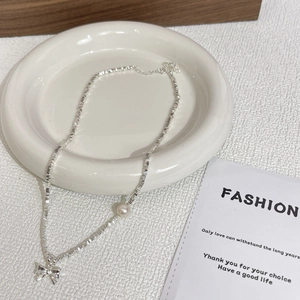 Detail of silver geometric chain featuring a white pearl and metallic bow pendant