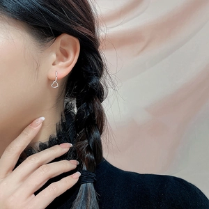 Détail de boucles d'oreilles argentées avec pendentif cœur évidé porté par un modèle