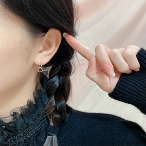 Boucles d'oreilles cœur évidé en argent portées par un mannequin sur fond rose doux