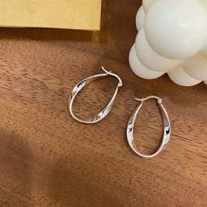 Boucles d'oreilles créoles géométriques argentées au design torsadé sur bois chaleureux