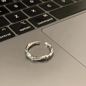 Irregular silver lava ring with blue resin accent on laptop keyboard, minimalist style
