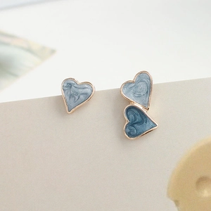 Detailed close-up of asymmetric heart stud earrings with blue marble enamel and gold trim